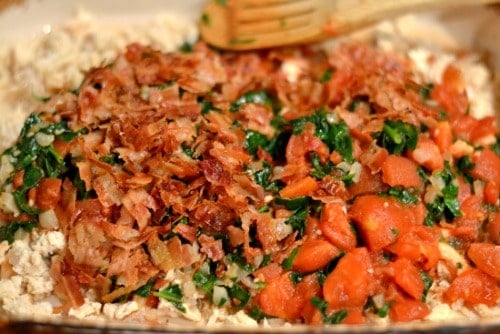 A close up of bacon pieces, tomatoes and spinach.