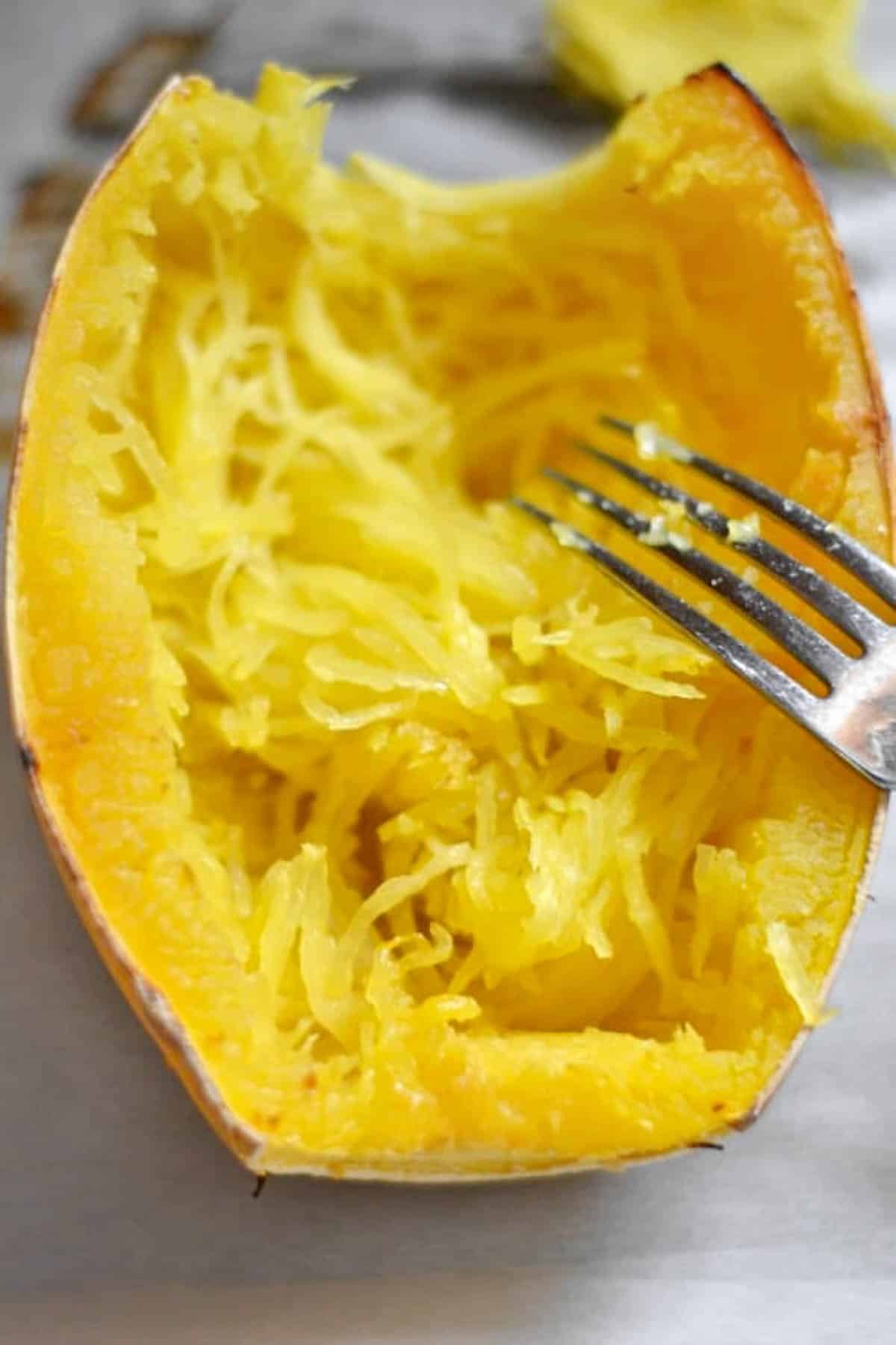 cooked spaghetti squash half with a fork scraping the inside 