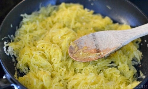 spaghetti squash in a pan being sauted with a wooded spoon