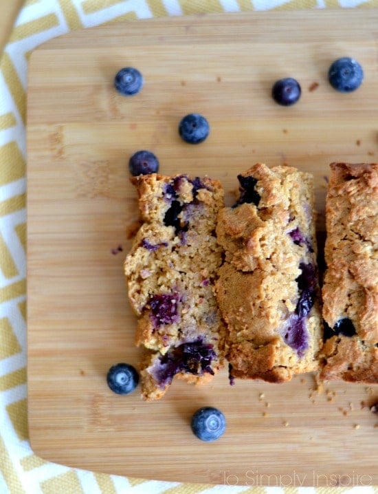 slices of blueberry bread on a wood cutting board surrounded by fresh blueberries