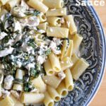 A big silver bowl with penne pasta topped with spinach and chicken mixture