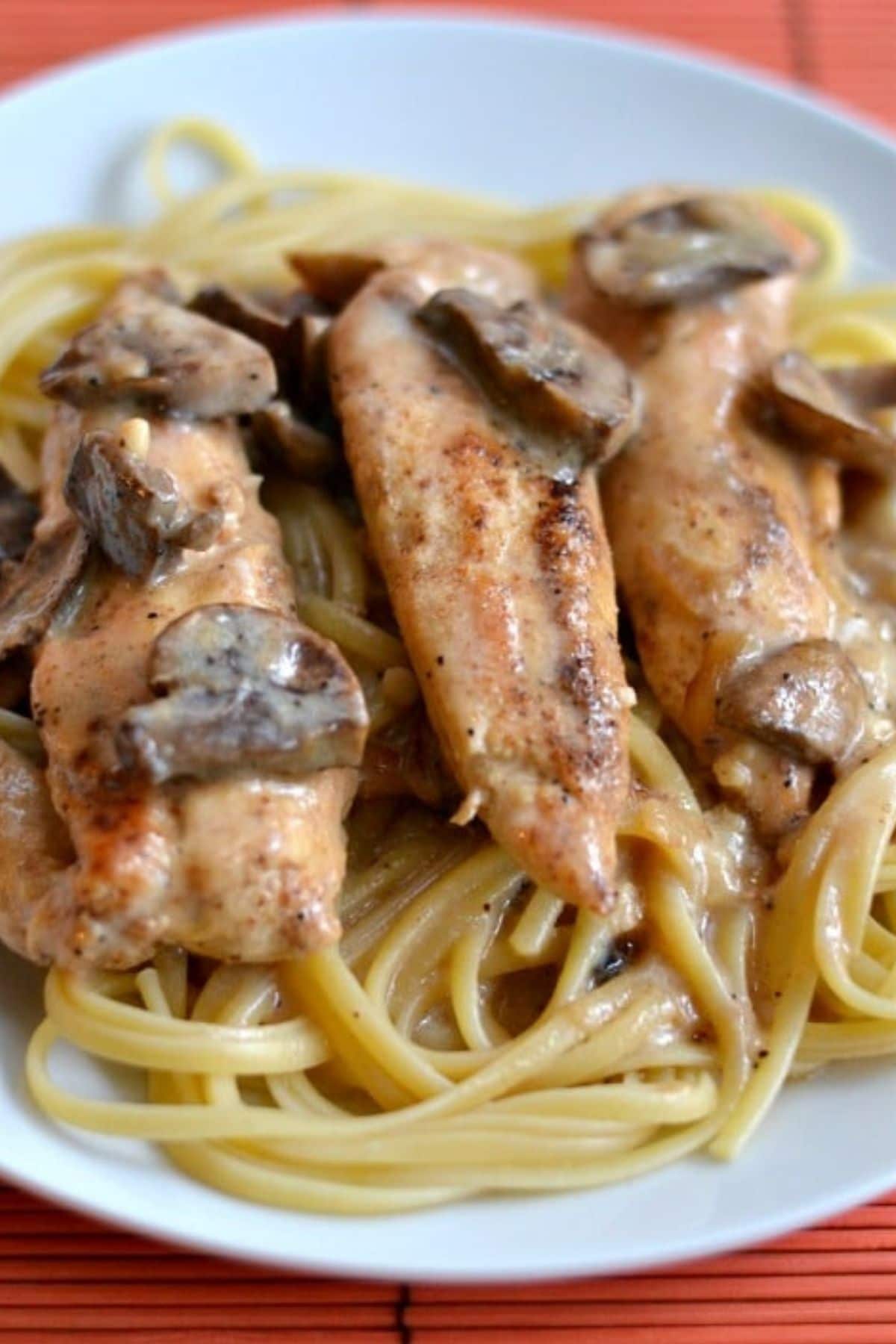 a white plate with spaghetti noodles topped with three chicken tenders and mushrooms.