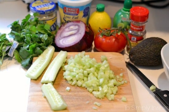 Cucumber Avocado Salsa Ingredients chopped celery on a wood cutting board surrounded by tomato, red onion, cilantro, lemon and spices