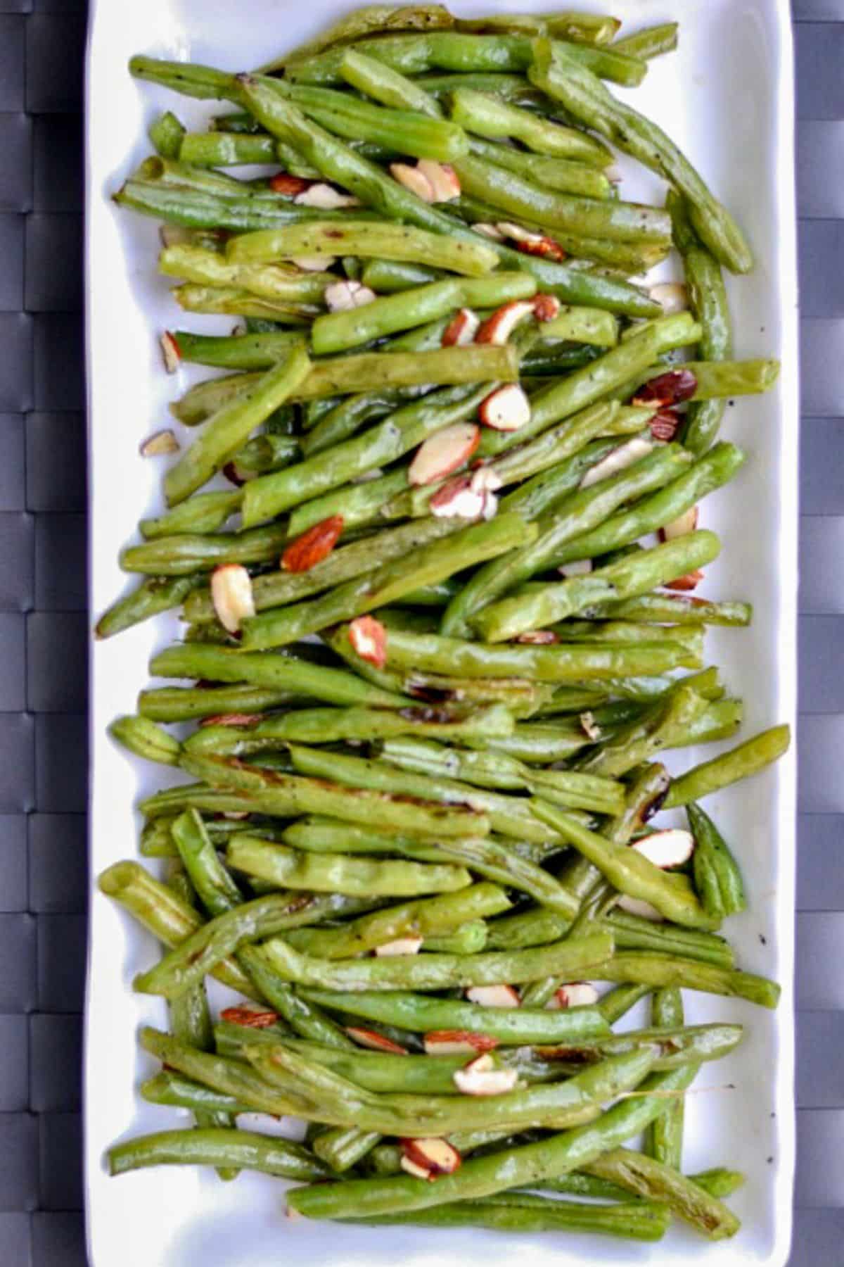 These roasted green beans are so simple and delicious with added sliced almonds. Add them to any meal as a wonderful, healthy side dish. roasted green beans topped with sliced almonds a white plate