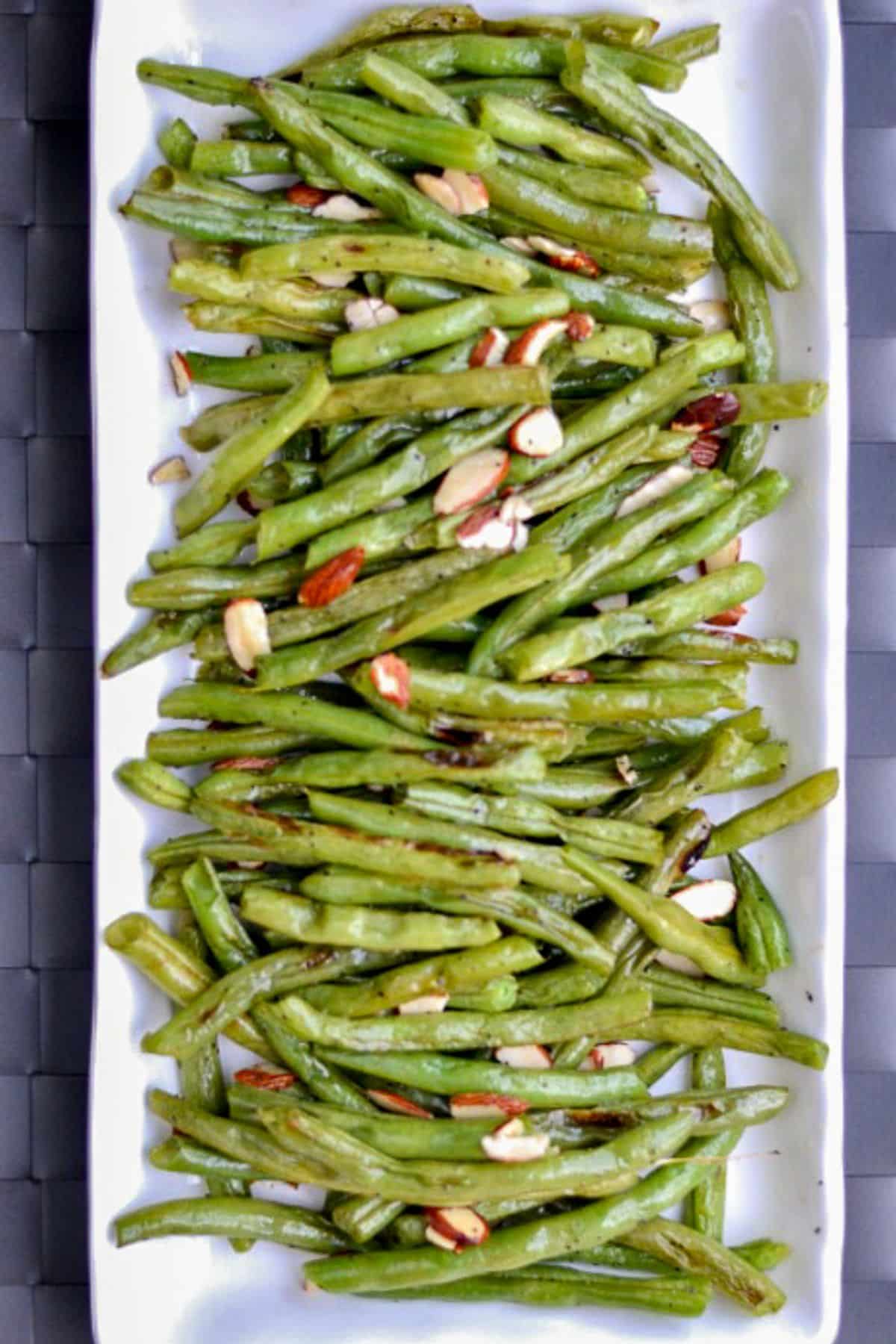 roasted green beans topped with sliced almonds a white plate 