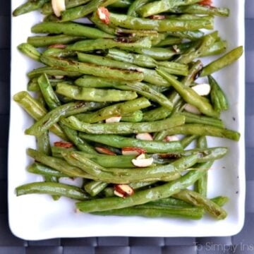 Roasted green beans recipe topped with sliced almonds on a white rectangle plate