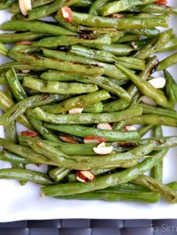 Roasted green beans recipe topped with sliced almonds on a white rectangle plate