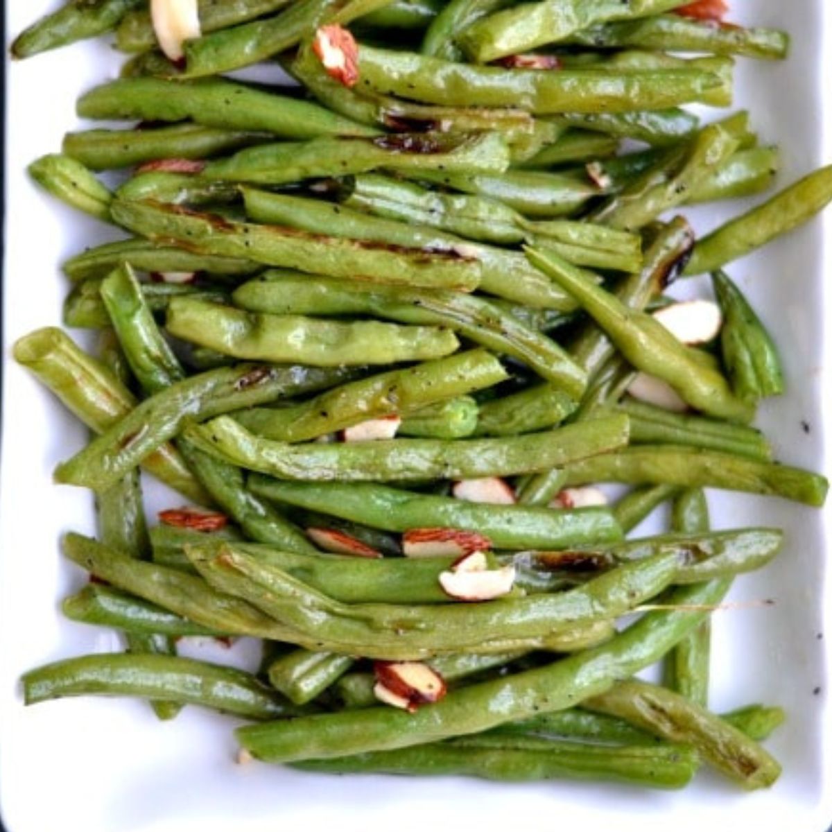 Roasted green beans recipe topped with sliced almonds on a white rectangle plate 