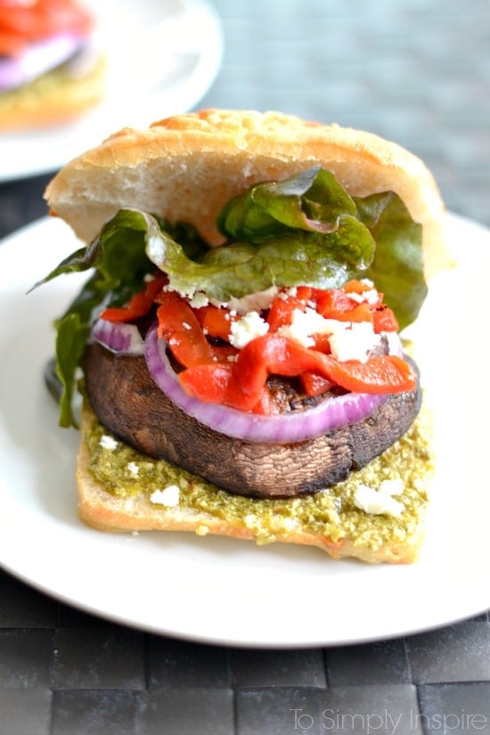 A close up of a open portobello Mushroom sandwich with lettuce, red peppers and red onion slice