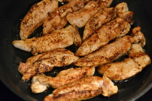 chicken tenders being sautéed in a black pan