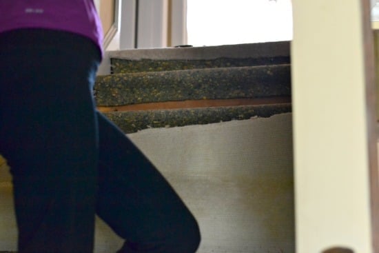 A person standing on stair pulling up carpet.