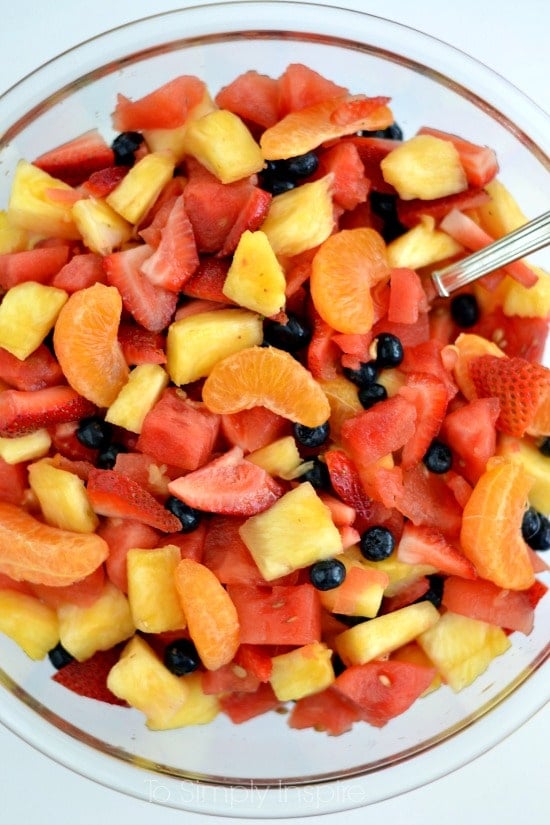 a big glass bowl filled with a mixture of oranges, watermelon, pineapple, strawberries and blueberries