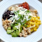 a white bowl with corn, avocado, black beans, salsa and cheese