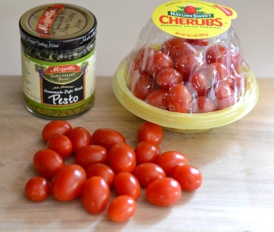 cherry tomatoes and a jar of pesto sauce on a cutting board