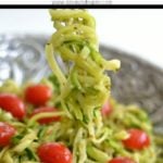 Pesto Zucchini Noodles on a fork in a big silver bowl