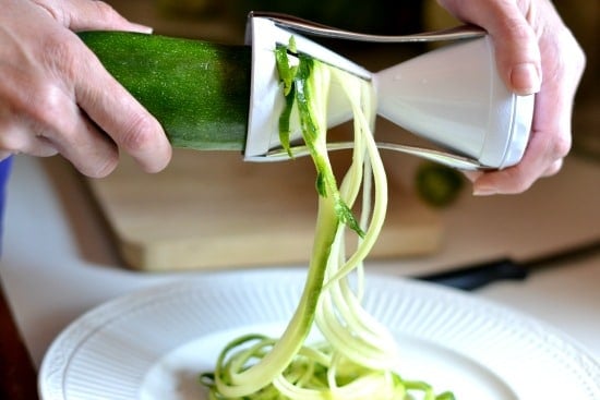 A person holding a spiralizer making zucchini noodles