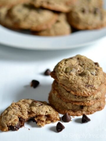 Oatmeal Chocolate Chip Cookies on a white table surrounded by chocolate chips with a plate in the background
