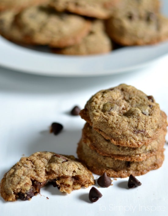  Oatmeal Chocolate Chip Cookies on a white table surrounded by chocolate chips with a plate in the background