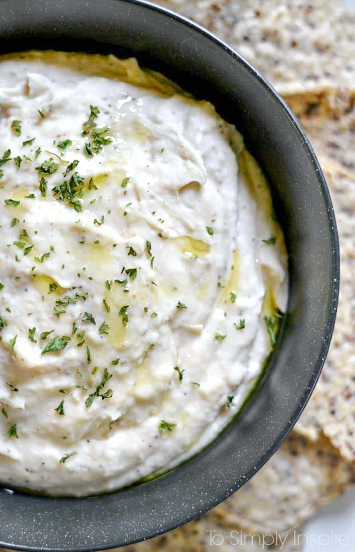 This White Bean Dip is an amazing creamy, healthy appetizer or even for lunch. Sautéed onions and garlic add an incredible, robust flavor. Grab your favorite veggies or crackers and dig in. White Bean Dip recipe in a bowl surrounded by chips on a plate