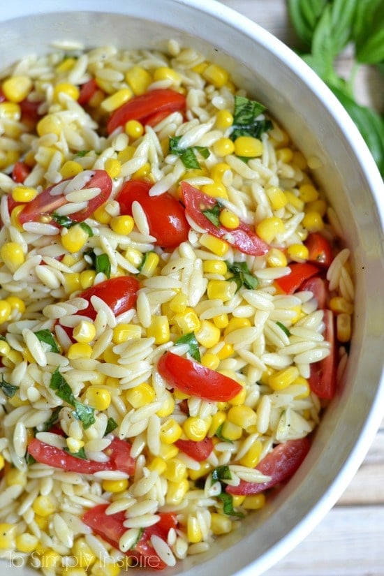 closeup of orzo pasta salad with sliced cherry tomatoes, corn and fresh basil
