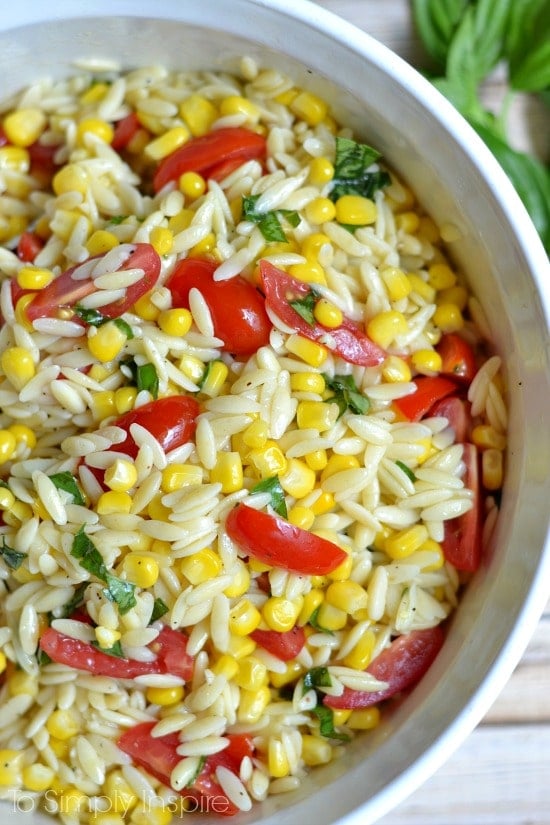 TThis Orzo Pasta Salad with roasted corn and sliced cherry tomatoes has loads of delicious flavors from simply adding fresh basil and garlic and tossing with a fabulous light lemony sauce. closeup of orzo pasta salad with sliced cherry tomatoes, corn and fresh basil