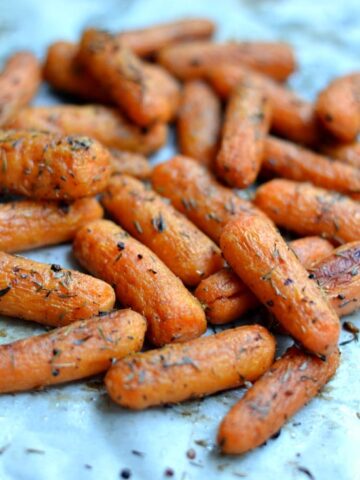 A pile of cooked baby carrots topped with herbs