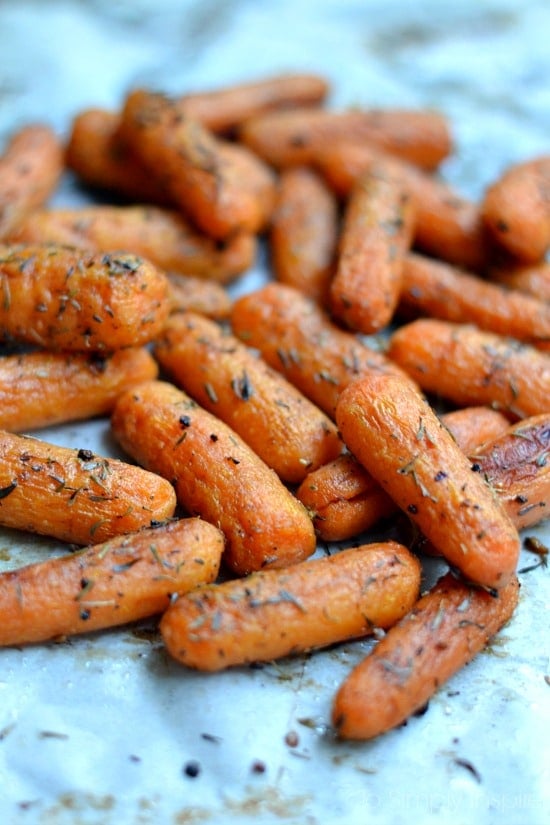 A pile of baby carrots topped with herbs on white parchment paper