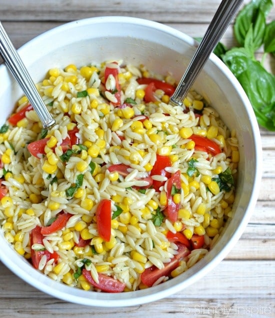 a white bowl of closeup of orzo pasta salad with sliced cherry tomatoes, corn and fresh basil