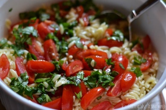 sliced cherry tomatoes and fresh basil on top of cooked orzo pasta