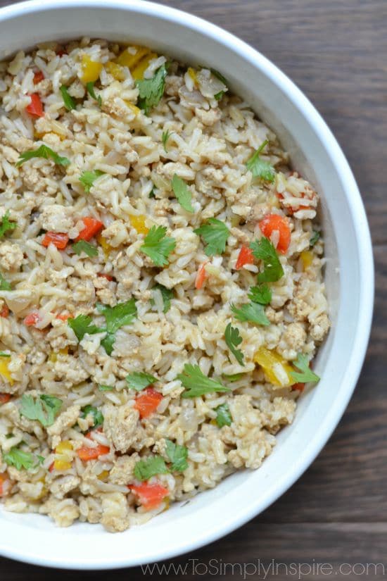 A close up of a bowl of brown rice with red and yellow peppers and cilantro pieces