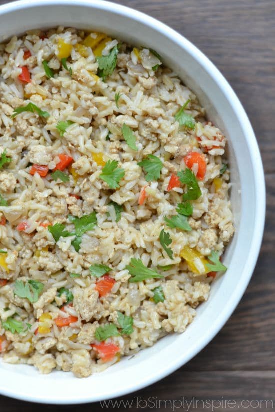 A close up of a bowl of brown rice with red and yellow peppers and cilantro pieces