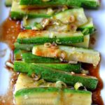 A plate full of zucchini slices topped in brown sauce and scallions