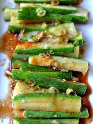 A plate full of zucchini slices topped in brown sauce and scallions