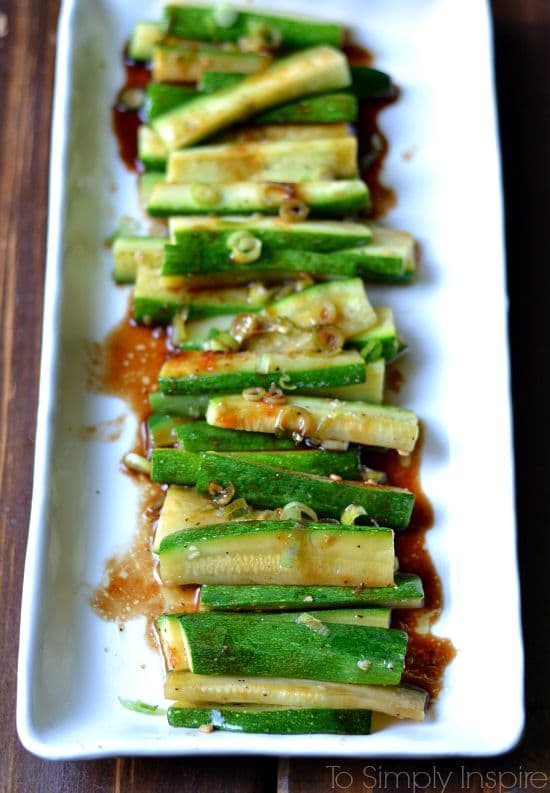 A white rectangle plate with zucchini slices in brown sauce and scallions 