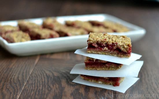 a stack of three strawberry oatmeal bars with a rectangle plate full behind