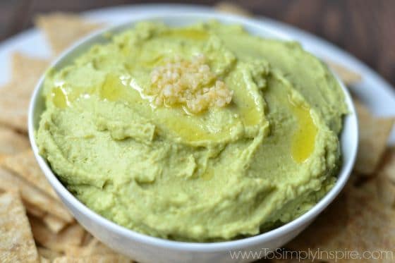 Avocado Hummus recipe in a white bowl surrounded by crackers.