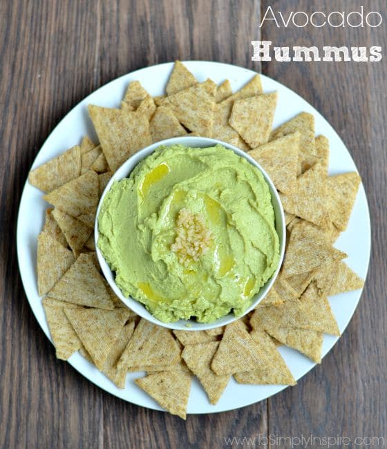 Avocado Hummus recipein a white bowl on a white plate surrounded by triscuit crackers