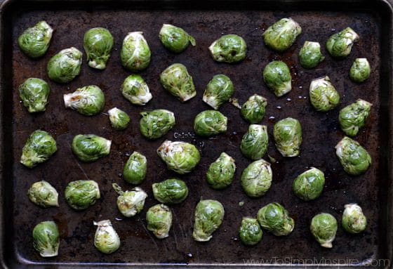 Uncooked sliced Brussel Sprouts spread on a baking sheet with balsamic vinegar