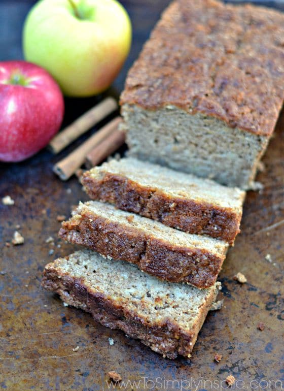 A close up of two slices of applesauce bread beside the loaf on a baking sheet with an apple 