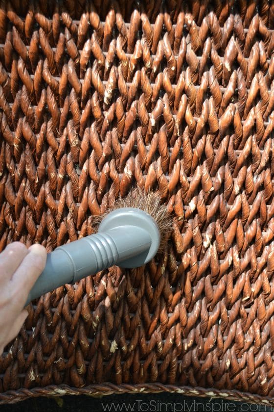 A close up of a brown wicker chair being vacuumed 