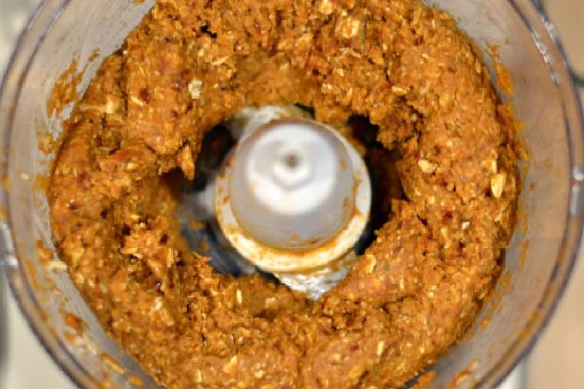 A close up of a food processor mixing ingredients for pumpkin pie bites