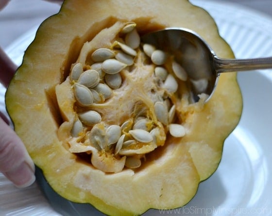 closeup of acorn squash with a spoon scooping out seeds