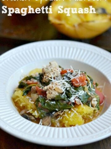 a white bowl with cooked spaghetti squash topped with cooked spinach, tomatoes, chicken and sprinkled with parmesan cheese