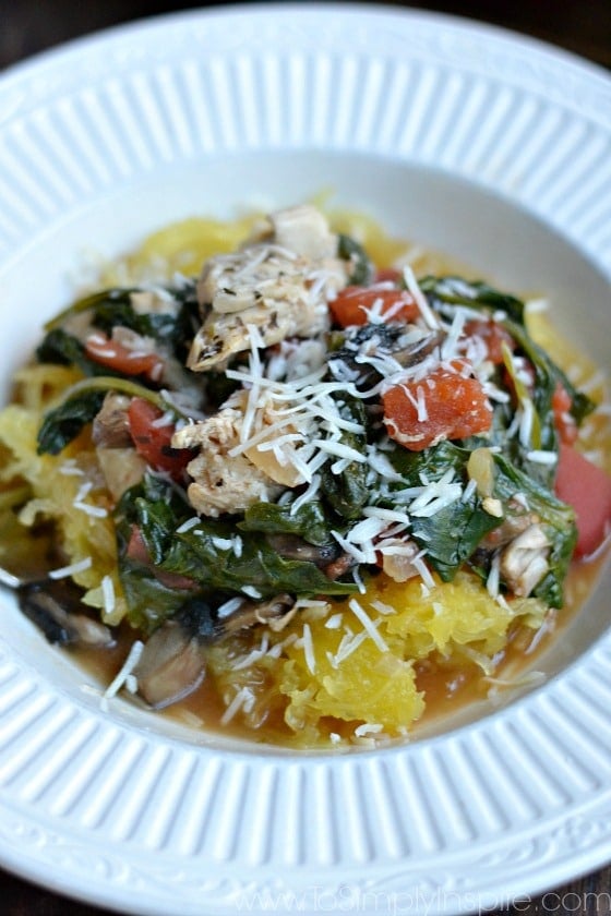 closeup of cooked spaghetti squash topped with cooked spinach, tomatoes, chicken and parmesan cheese in a bowl
