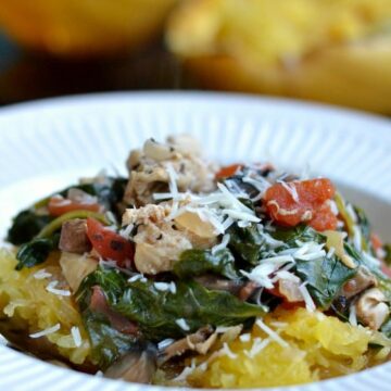 a white bowl with cooked spaghetti squash topped with cooked spinach, tomatoes, chicken and parmesan cheese