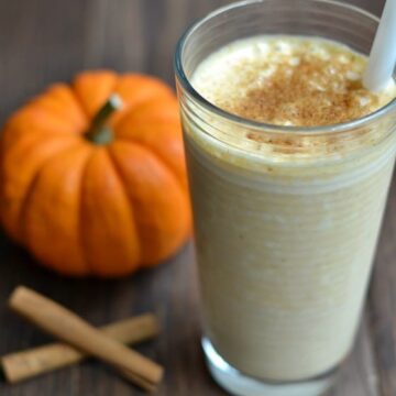 a glass of pumpkin smoothie with a small pumpkin