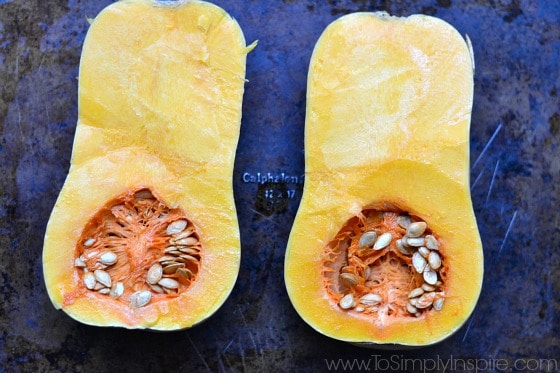 a whole butternut squash cut in half with seeds inside on a baking sheet