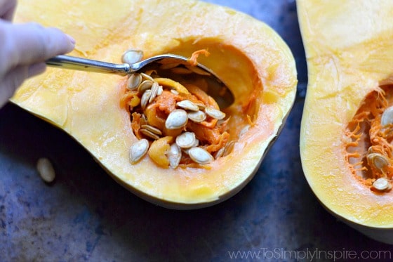 half of a butternut squash with the seeds being scooped out with a spoon