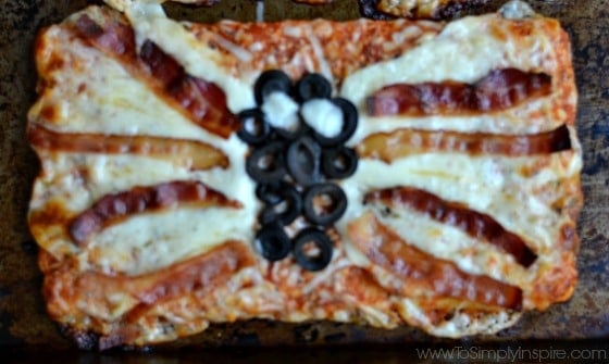 A slice of pizza with cheese, olives and bacon slices made in the shape of a spider