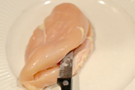 raw Chicken Breast being sliced in half with a knife